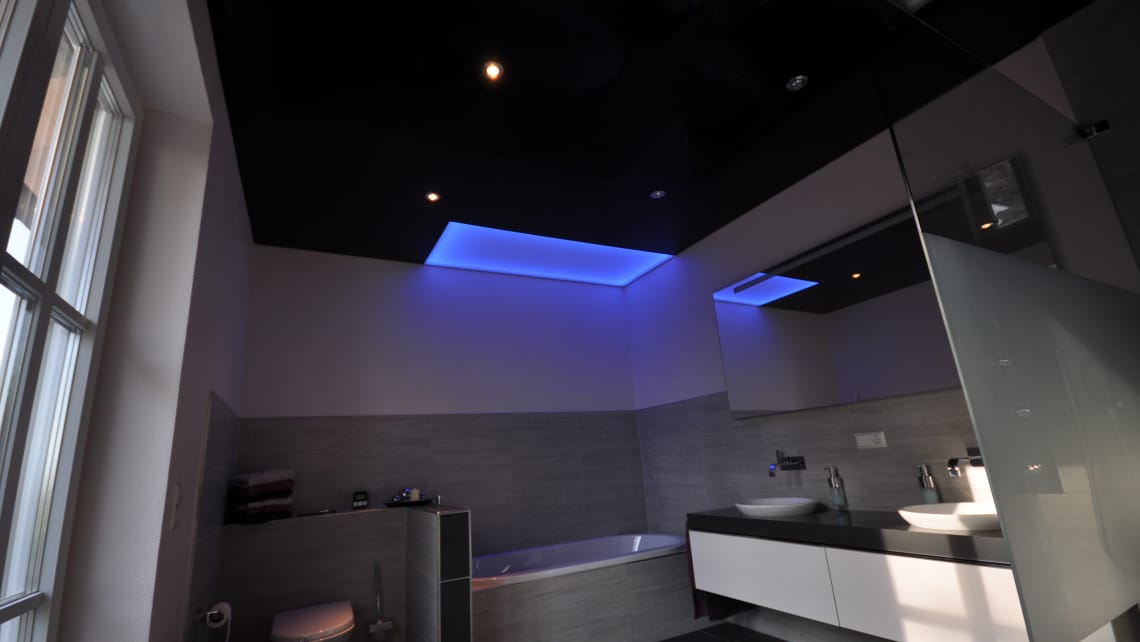 Lackspanndecke in schwarz Hochglanz im Bad mit LED-Einbaustrahlern und Deckenfeld als Lichtdecke in LED-RGB