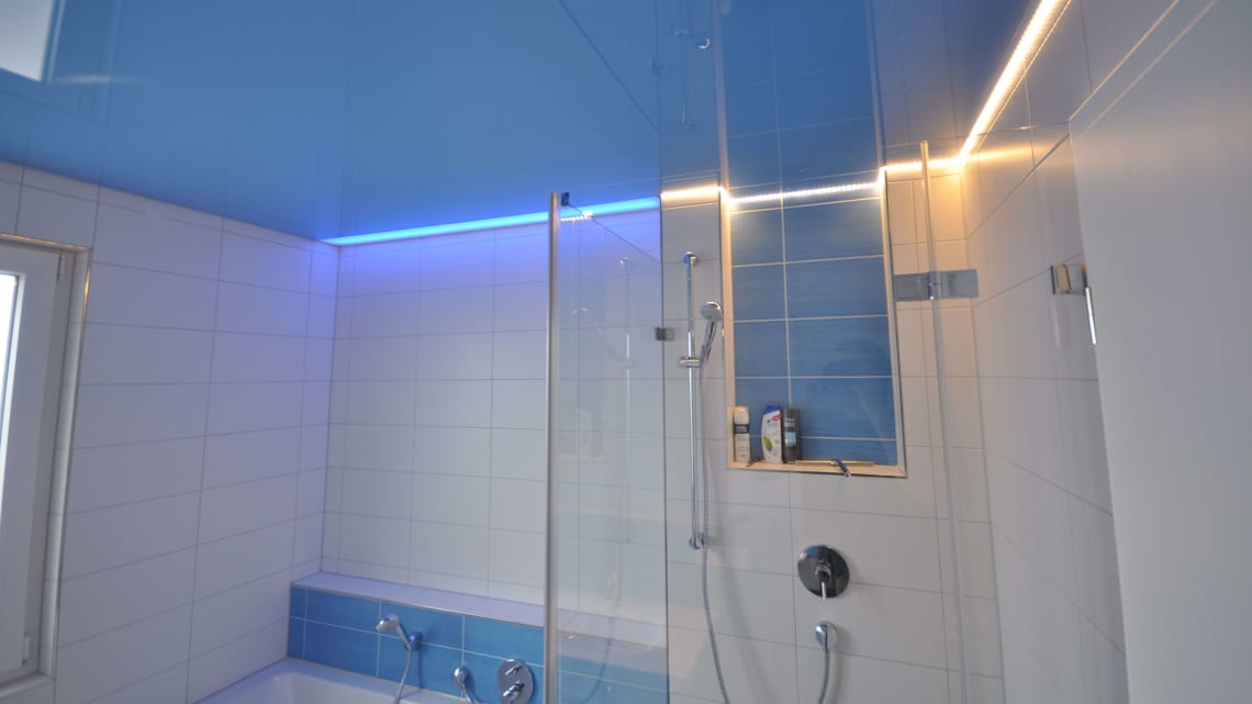 Lackspanndecke im Bad mit Lichtdecke über den Badewanne in hellblau Hochglanz. Beleuchtung mit LED-Einbaustrahlern, LED-Lichtkanal in der Schattenfuge und LED-RGB Band hinter der Spanndecke über der Wanne