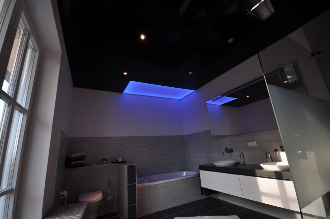 Lackspanndecke in schwarz Hochglanz im Bad mit LED-Einbaustrahlern und Deckenfeld als Lichtdecke in LED-RGB