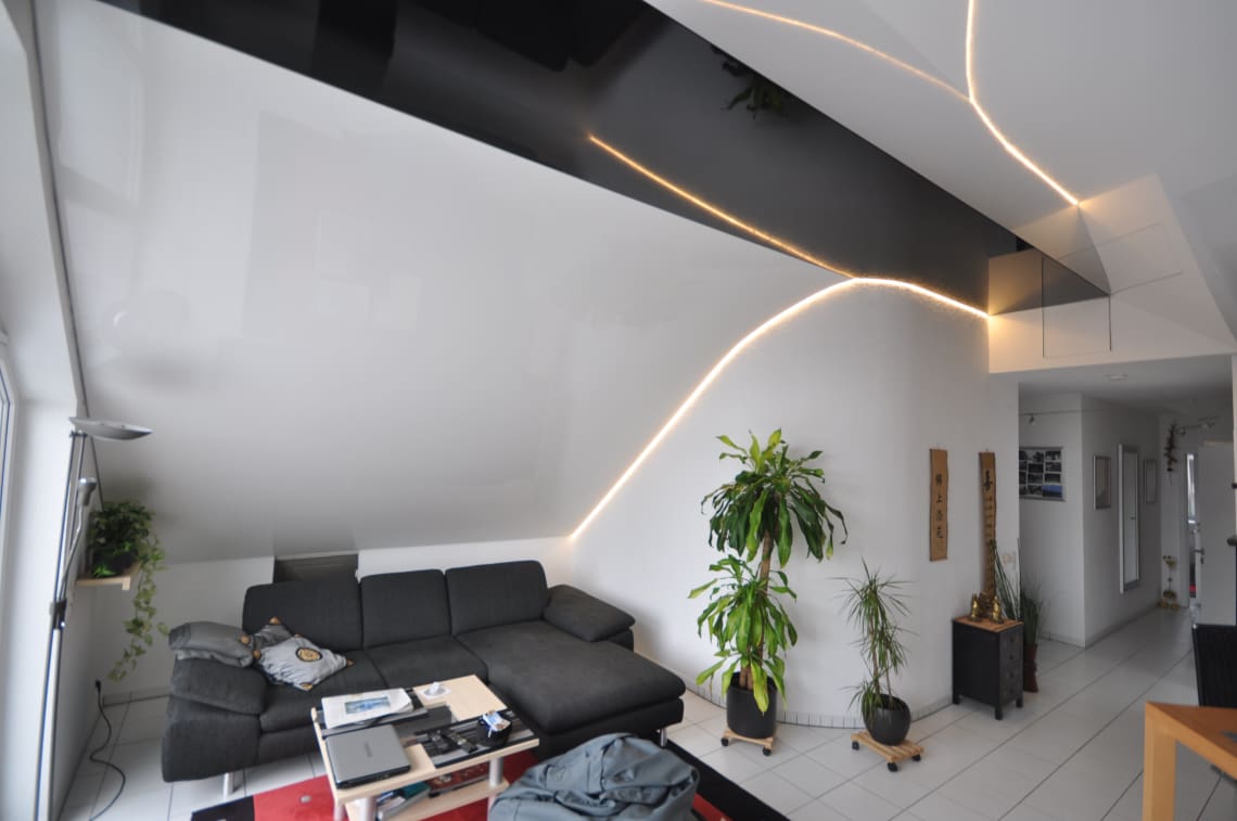 Lackspanndecke im Wohnzimmer mit Dachschräge in schwarz und weiss Hochglanz. Beleuchtung mit LED Band in der Schattenfuge dimmbar